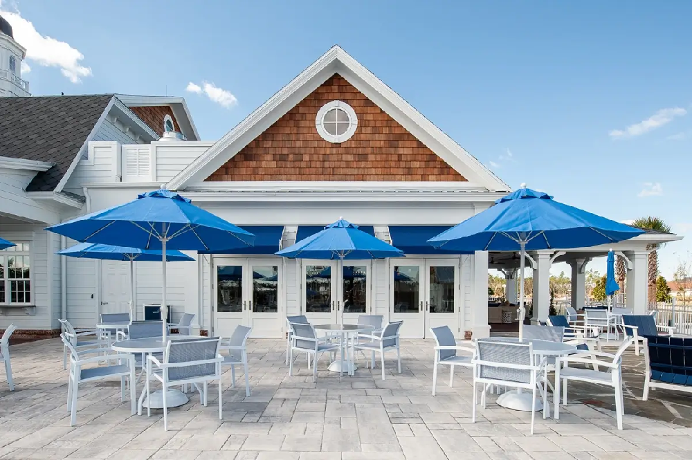 Community clubhouse patio featuring white Micamy dining chairs and royal blue Frankford umbrellas for shaded poolside dining and conversation.